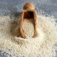 Raw uncooked fonio seeds with a spoon on grey background close up