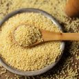 Millet groats in spoon above bowl, top view