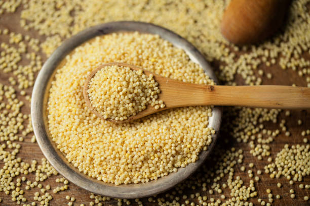 Millet groats in spoon above bowl, top view